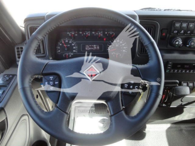 Truck cabin steering wheel and dashboard visible in International MV cab; gauges and controls on dash; watermark overlay across image.