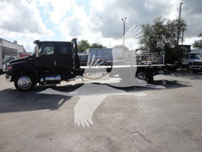 Truck cab and long flatbed rollback w/ dual rear axles, black color, side view showing International MV label? visible text not clear.