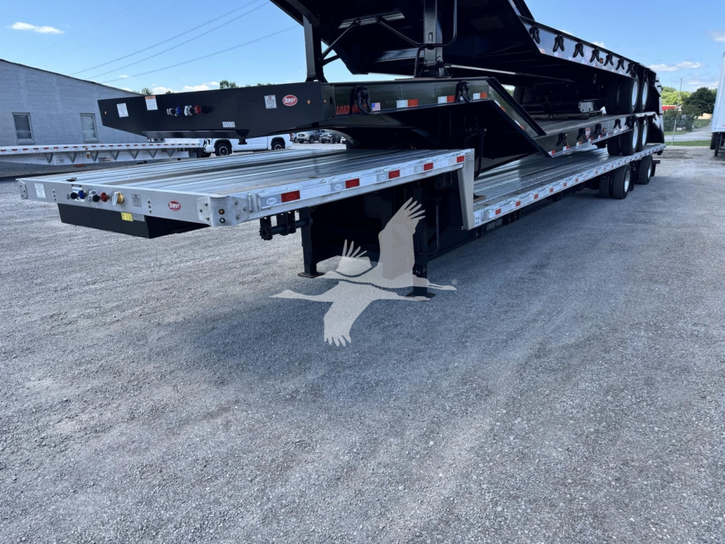 Trailer showing drop deck multi-axle trailer with extendable ramp and metallic silver cross members visible.