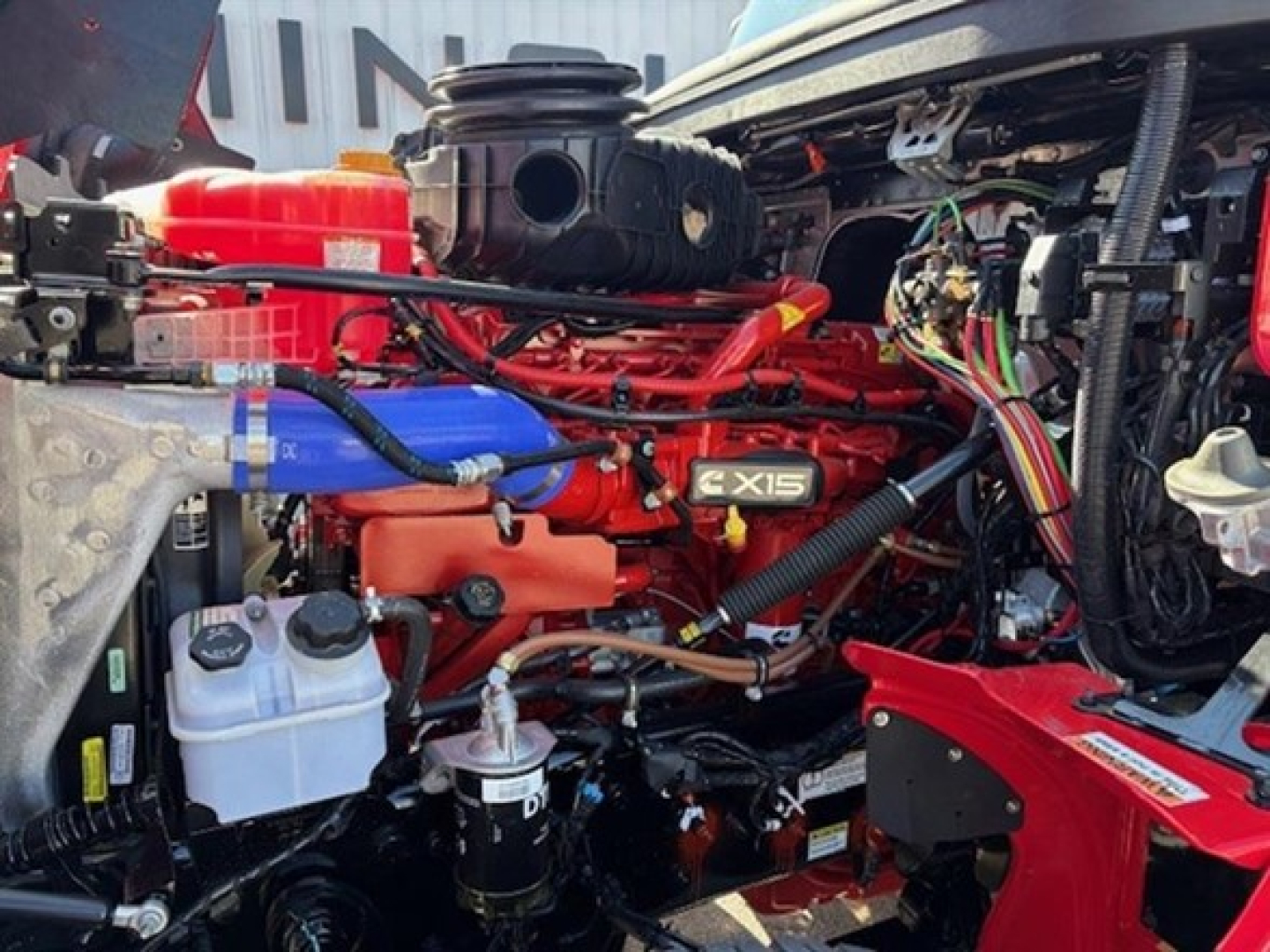Western Star 49X engine bay showing Cummins X15 diesel engine with red components, blue hoses, and multiple labeled fluid reservoirs and wiring harnesses.