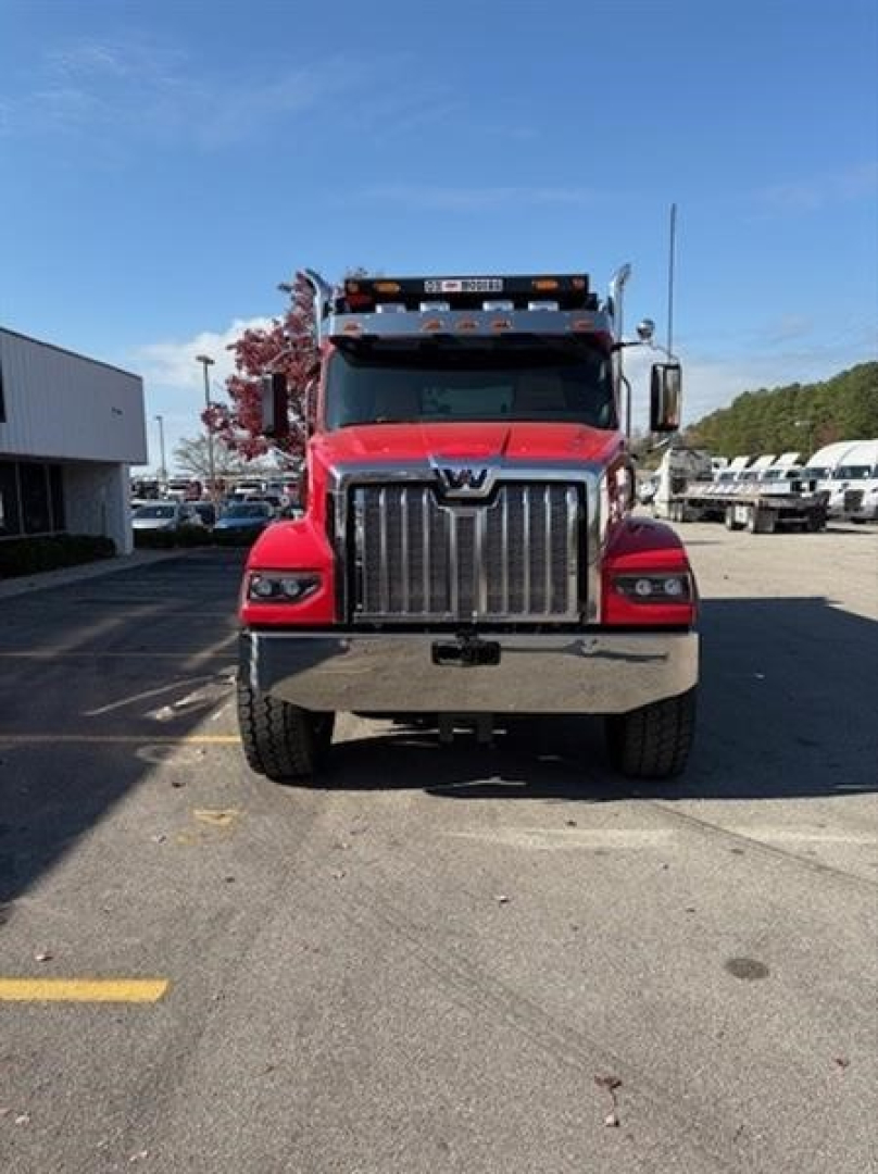 Front view of a red 2026 Western Star 49X truck in a dealership lot, showing the bold chrome grille, large bumper, and headlamps.