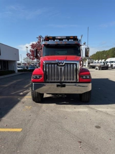 Front view of a red 2026 Western Star 49X truck in a dealership lot, showing the bold chrome grille, large bumper, and headlamps.