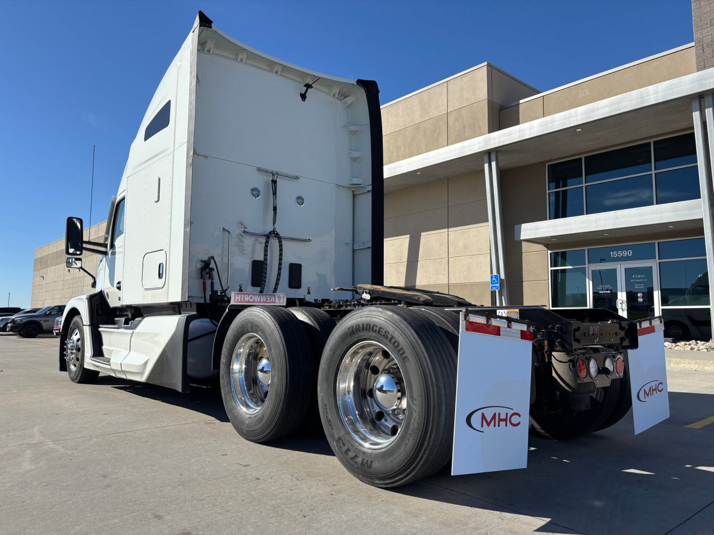 Kenworth T680 truck rear view showing dual rear axles and white cab with mud flaps and chrome wheels.