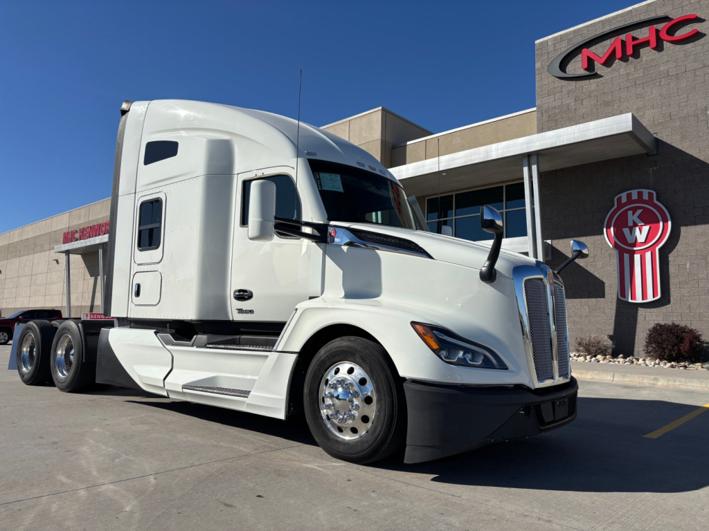 Kenworth T680 truck in front view with sleeper cab, white exterior, dealership in background.