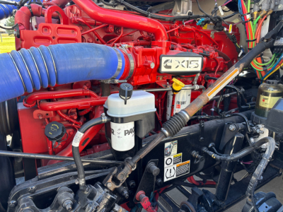 Kenworth T680 engine bay showing coolant reservoir, Dexron-style fluid lines, and red engine hardware with a white badge reading X15.