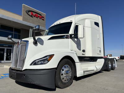 Kenworth T680 highway truck front-left view with white cab, chrome grille, and dual rear axles, dealership backdrop.