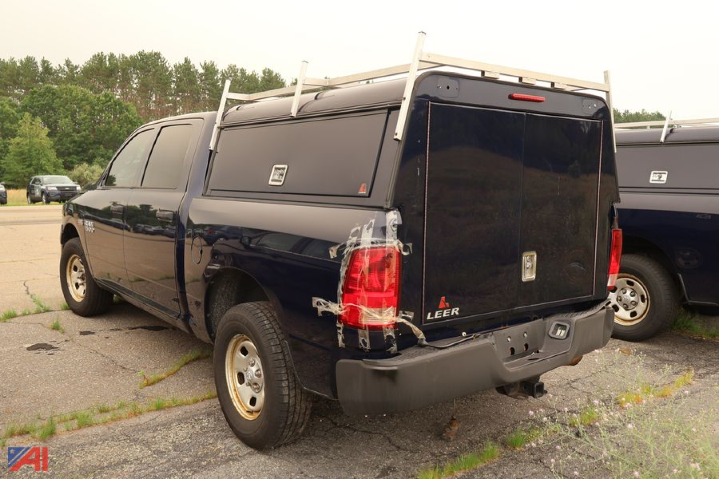 Ram 1500 pickup with cap showing rear and left side, black cap over truck bed, tail lights, ladders on top, parking lot.