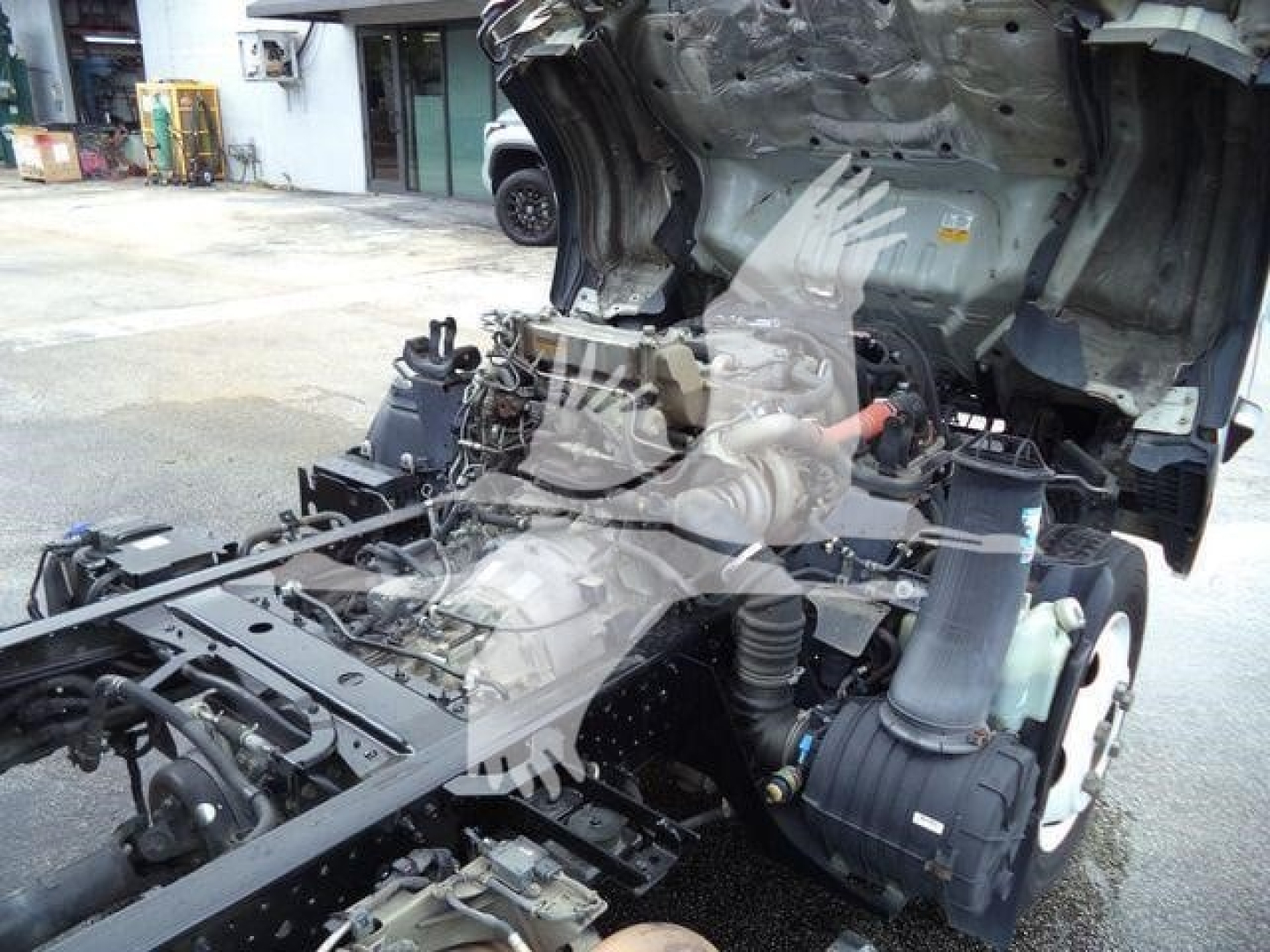 Isuzu NPR XD truck chassis with exposed engine and drivetrain components visible, from a partial side view.