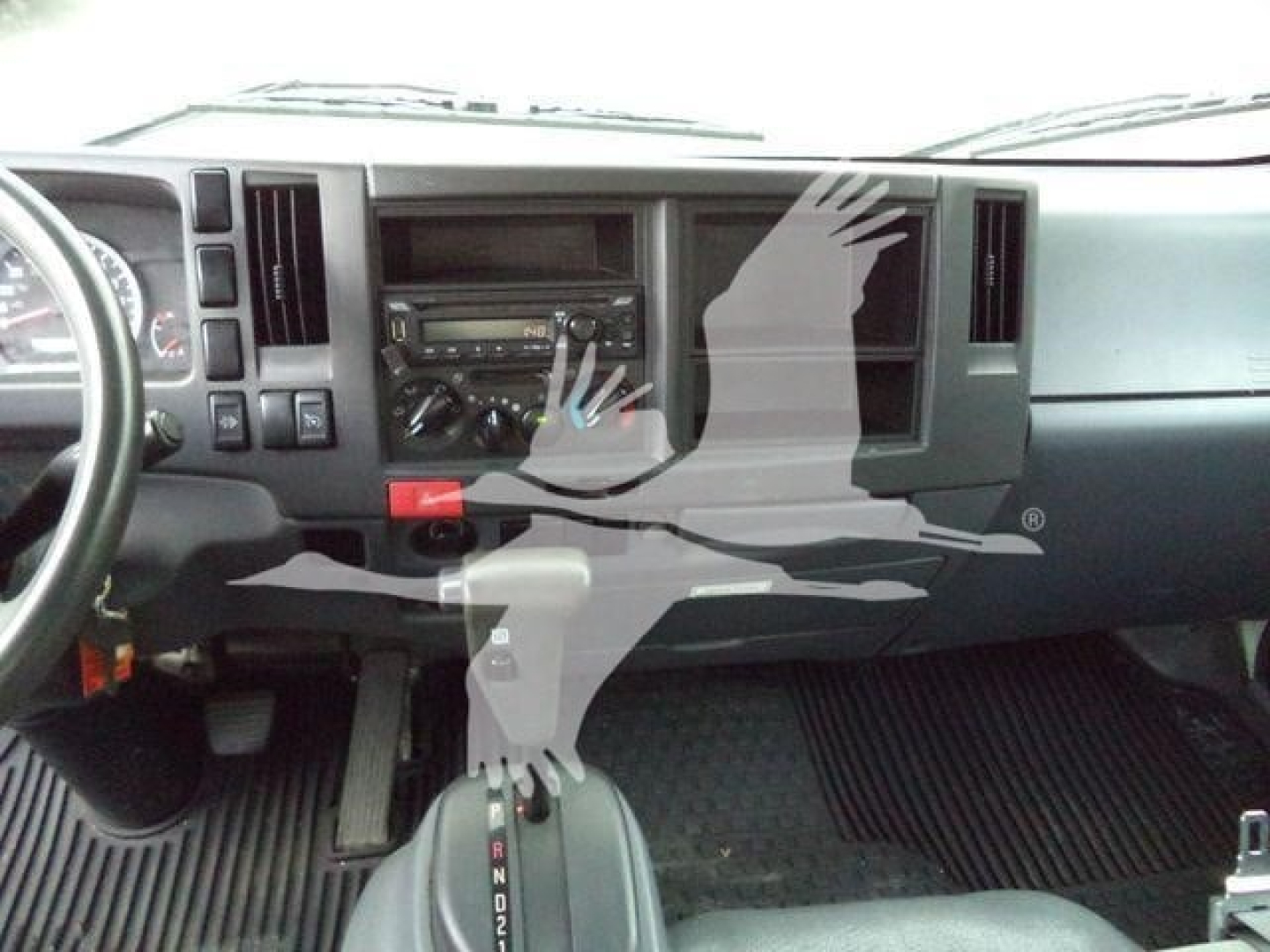 Isuzu NPR-XD dashboard and center console with gear shift visible and steering wheel on left; dashboard shows standard radio and climate controls.