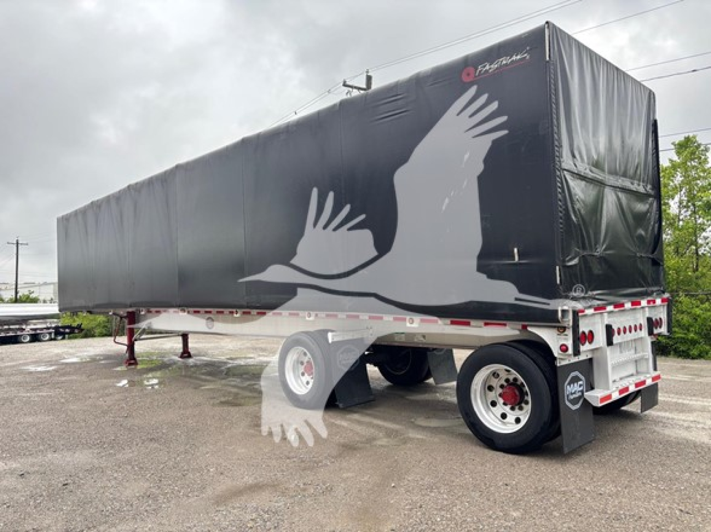Curtainside trailer with black tarp showing white bird graphic, side view, MAC branding on front, rear mud flaps, undercarriage visible.