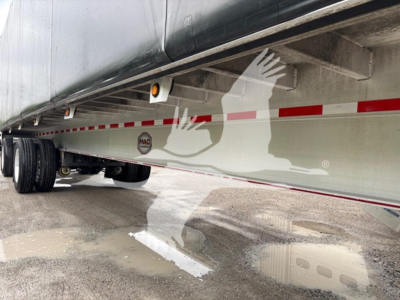 Trailer side view showing MAC logo and reflective strip underneath curtainside trailer, undercarriage and wheels visible.