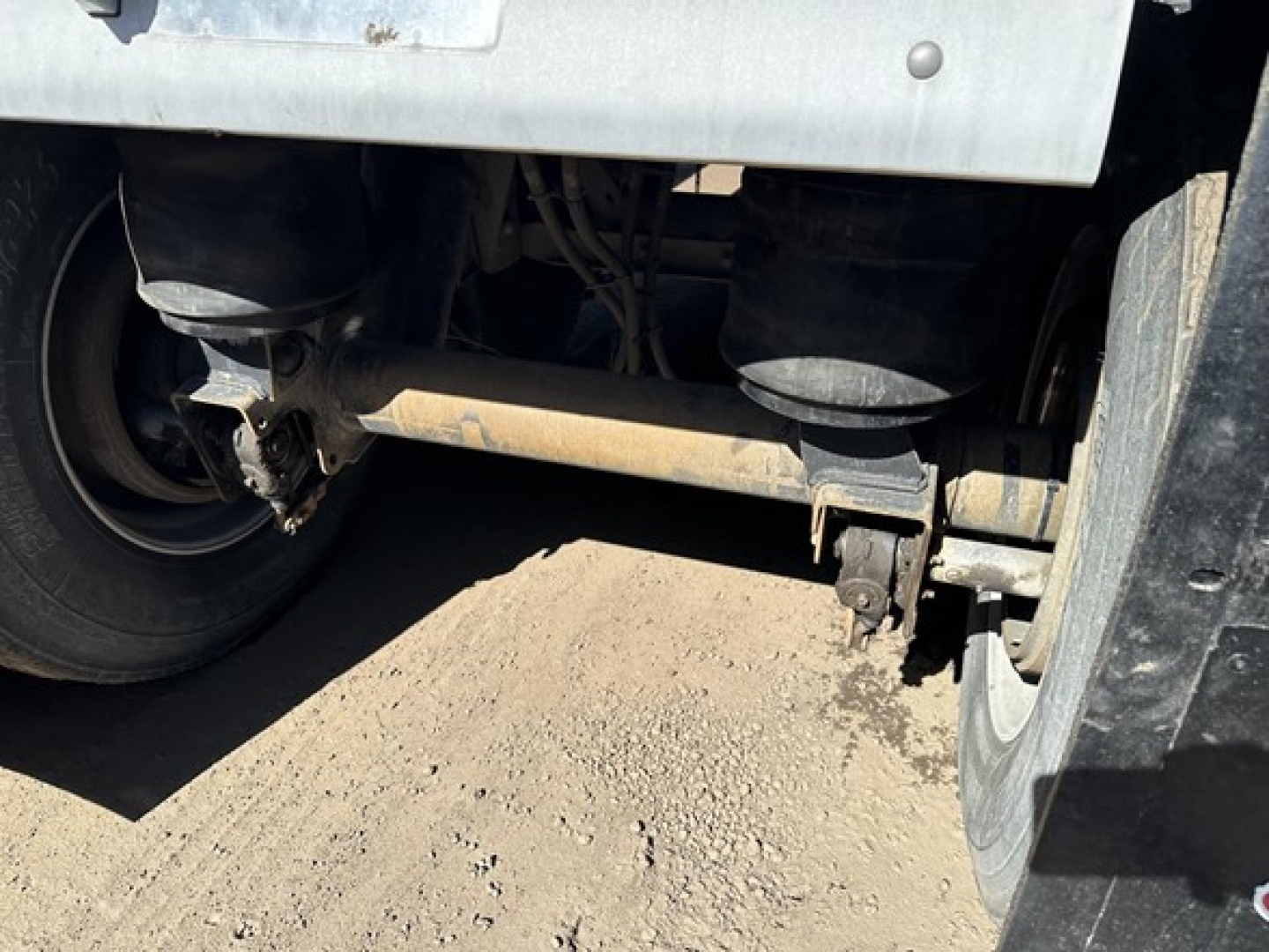 Rear underside of 2017 Mac trailer showing axle, suspension components, and part of the frame with dirt and grime.