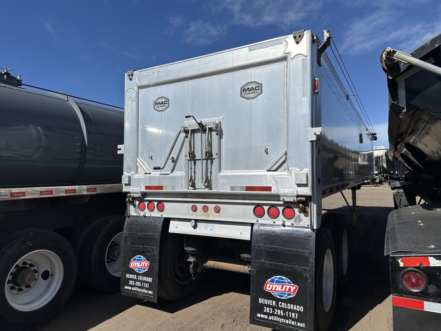 Mac MVP dump trailer rear showing dual mac decals on doors, metal latch, and red/white taillights with mud flaps and Utility Colorado dealer plate.