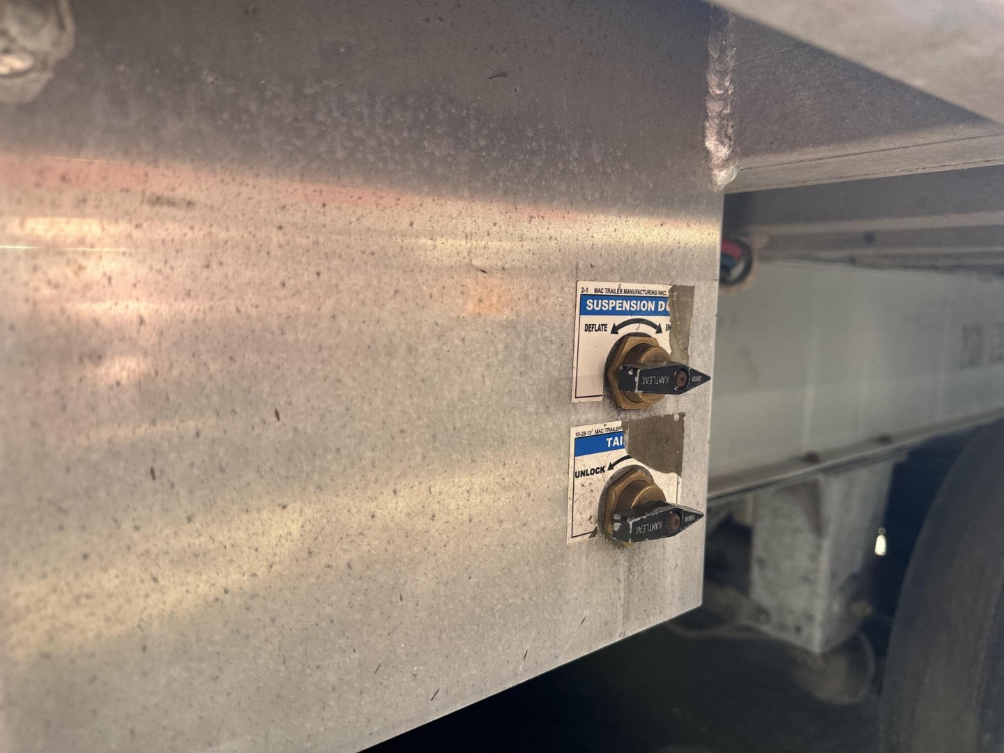 Trailer frame with two labeled levers for suspension control; metal panel with small blue-and-white labels and black knobs.