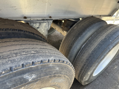 Dual trailer tires mounted under a dump trailer frame with mud and wear on tread.