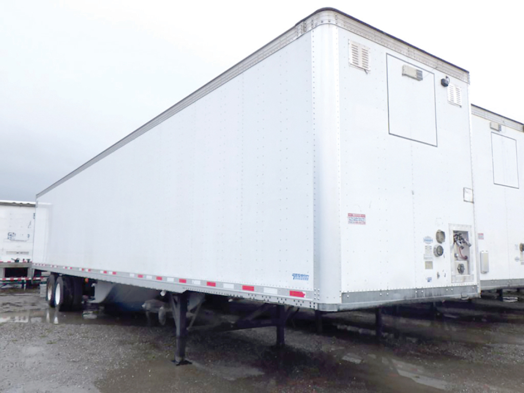 Trailer side view showing a white Vanguard trailer with undercarriage, support legs, and rear access door. VIN tag and stock number not legible.