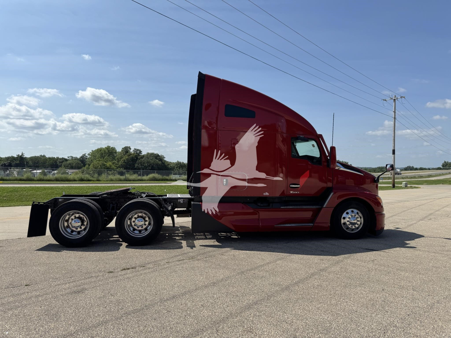 Kenworth T680 tractor trailer in red with side graphics, side view showing cab and dual rear axle without trailer.