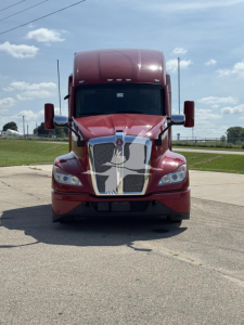 Front view of a red 2023 Kenworth T680 conventional sleeper truck with large chrome grille and badges.