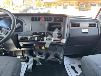 Truck cab interior of a 2023 Kenworth T680 with steering wheel, dashboard controls, gear shifter, and cup holders visible.
