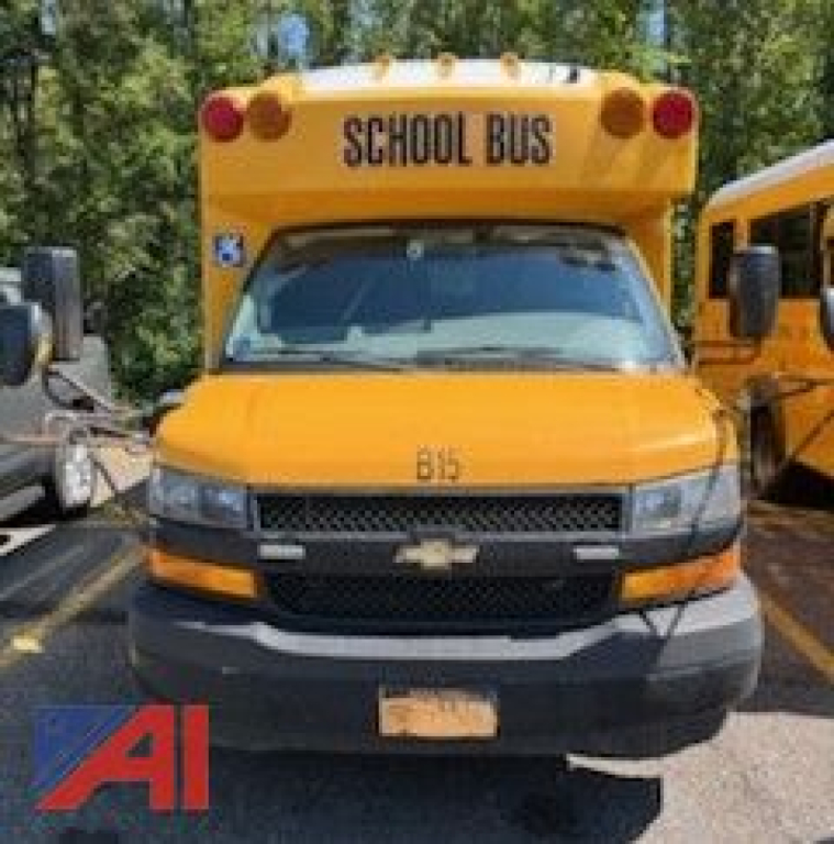 School bus front view showing Chevrolet grille and windshield; top sign reads SCHOOL BUS; yellow body with bumper and headlights visible.