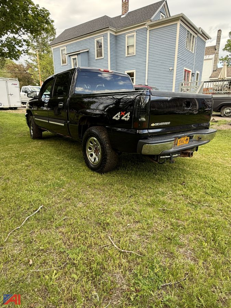 Chevrolet Silverado 1500 extended cab pickup truck in black, rear view showing 4x4 badge, long bed, NY license plate, blue house in background.