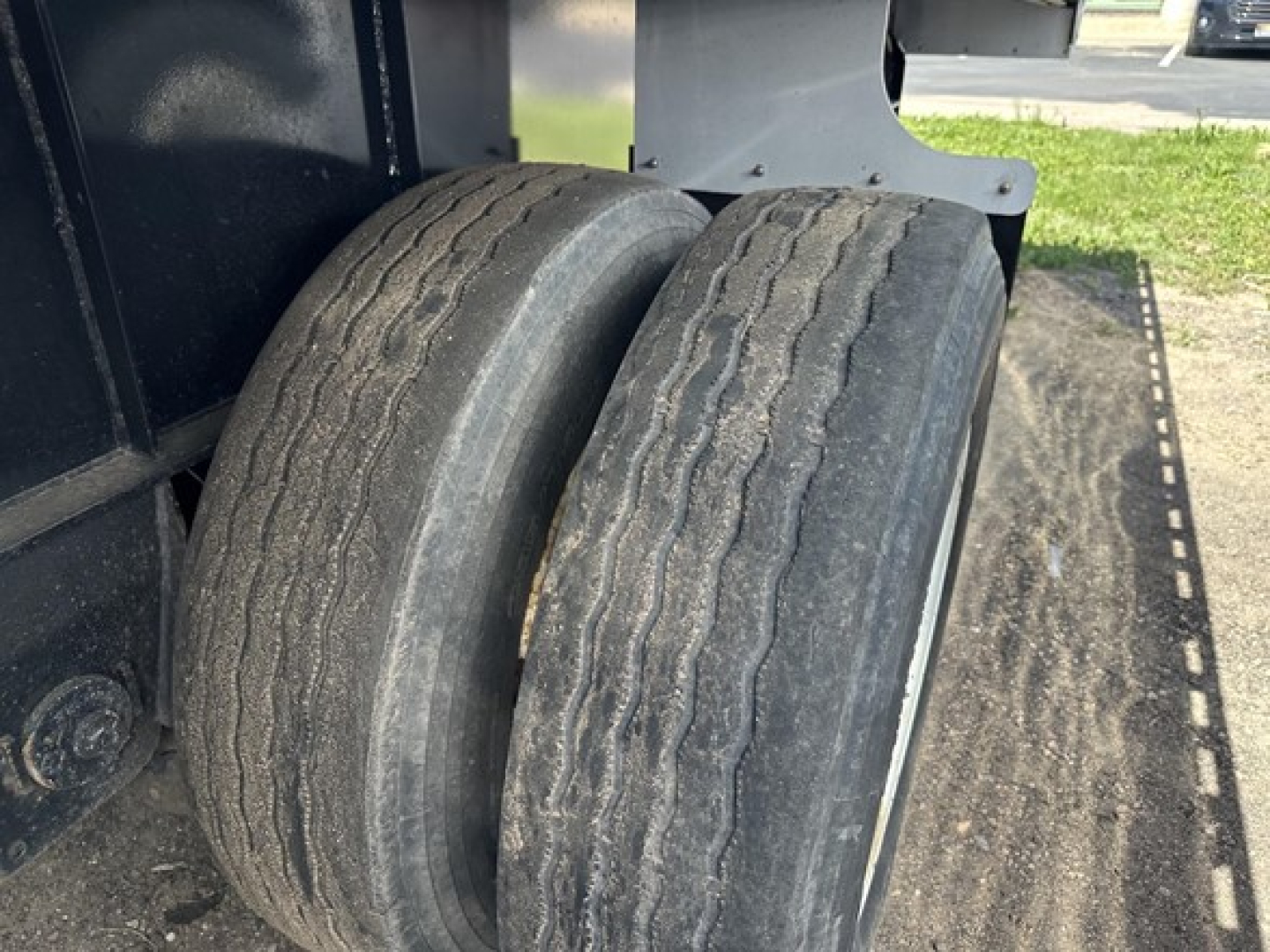 Two tires on a Transcraft trailer with a flatbed; visible wear on tread and sidewall details; part of chassis and deck in background.