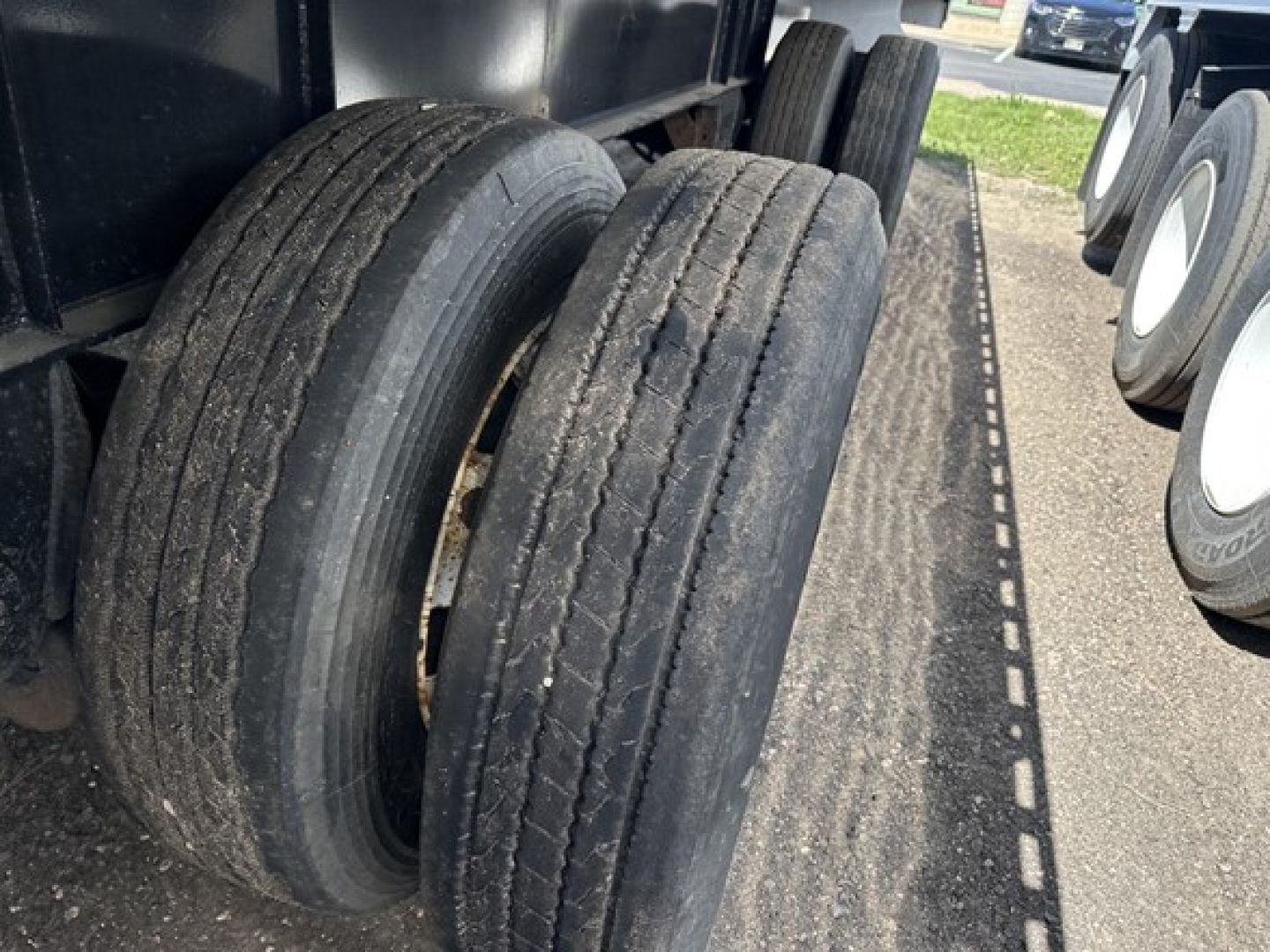 Truck trailer axles with dual rear tires on a flatbed, showing wear on tread and surrounding trailer deck.