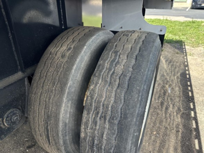 Two tires on a Transcraft trailer with a flatbed; visible wear on tread and sidewall details; part of chassis and deck in background.