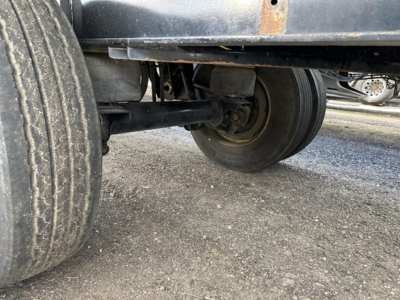 Trailer axle and wheels under a Transcraft spread air combo flatbed showing dual rear axles and air brake components.