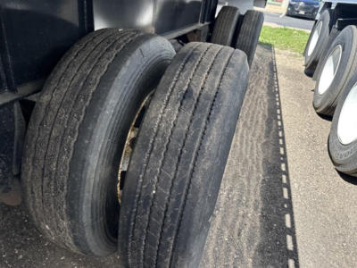 Truck trailer axles with dual rear tires on a flatbed, showing wear on tread and surrounding trailer deck.