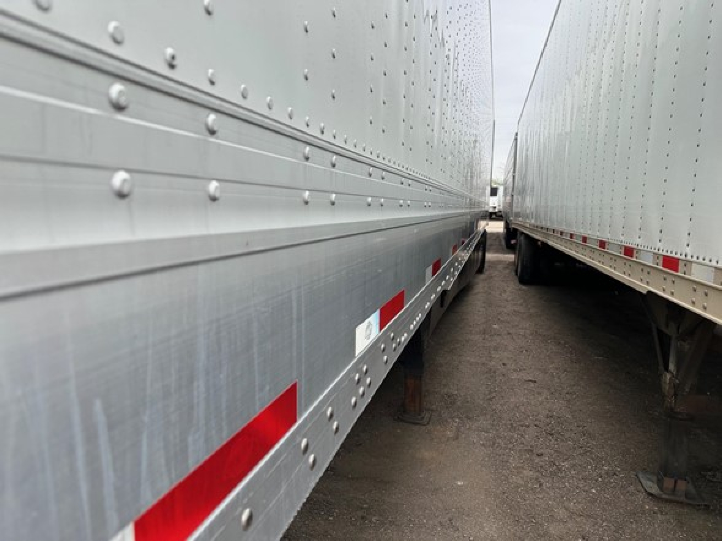 Trailer side view showing silver metal sides with rivets and reflective red/white stripes along the lower edge.