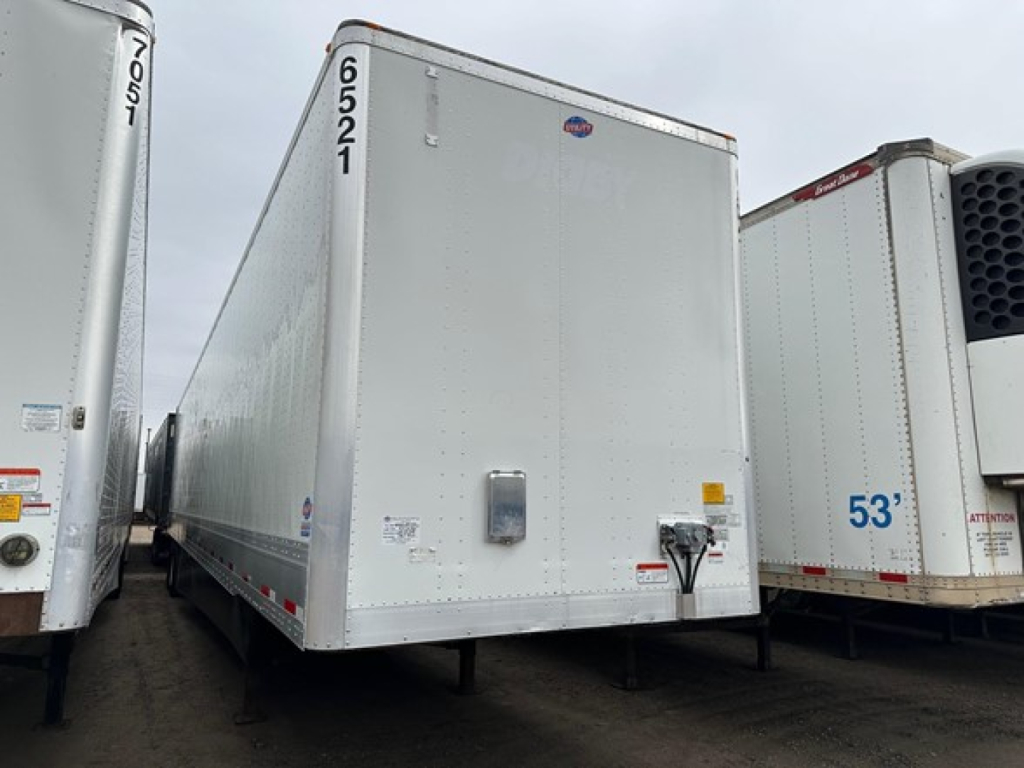 Trailer side view showing a white Utility 4000DX box trailer with number 6521 and 70105 markings, dock height feet not visible, front corner details and hitch area.