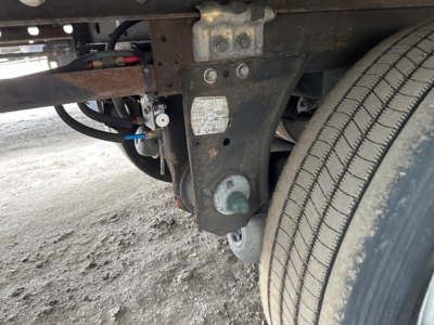Trailer undercarriage showing wheel, leaf spring, and electrical connections near the frame with a gray caster wheel and scattered labels.