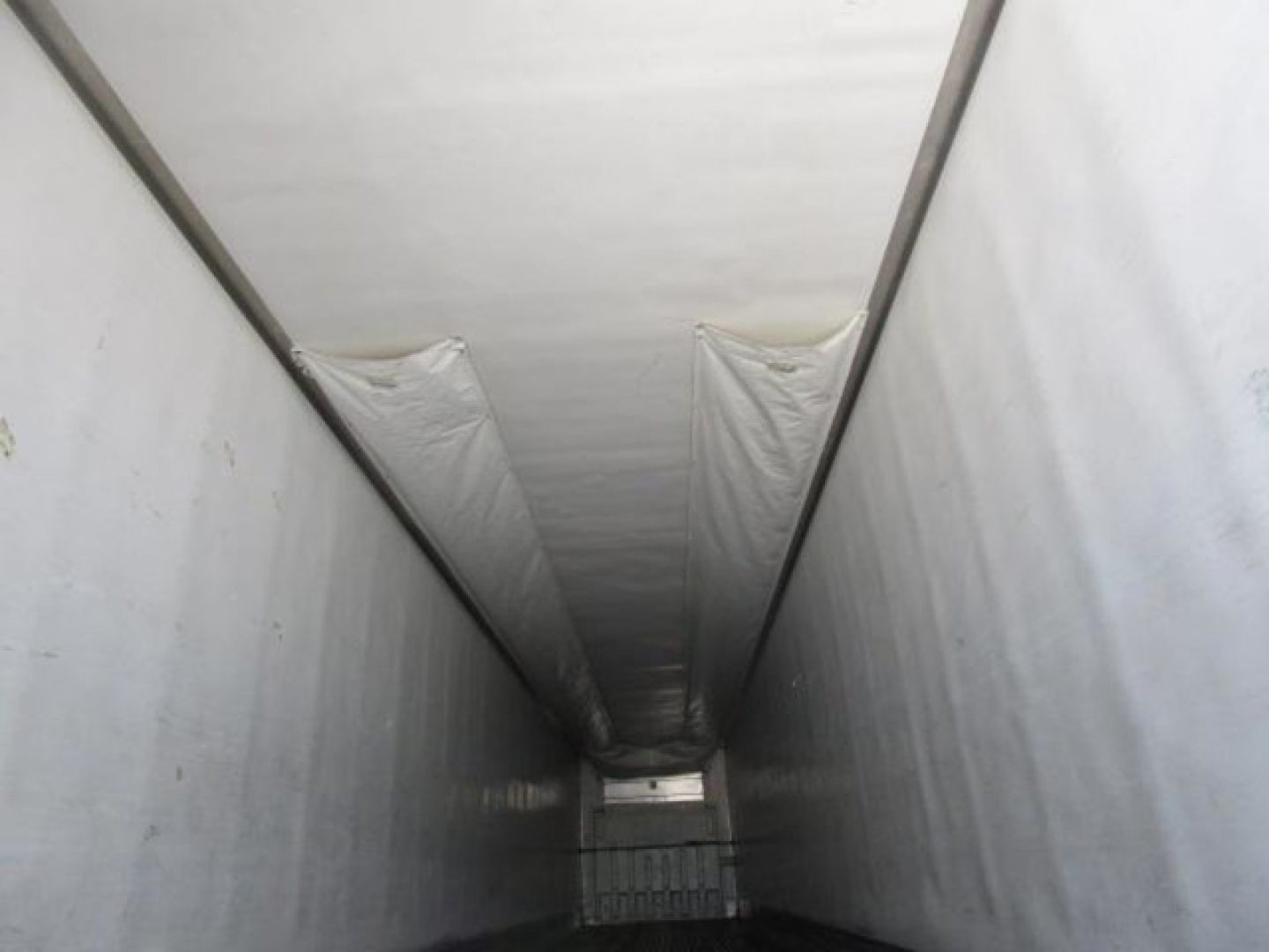 Trailer interior looking down a refrigerated trailer niche with white walls and ceiling, narrow passage, cargo door at far end.