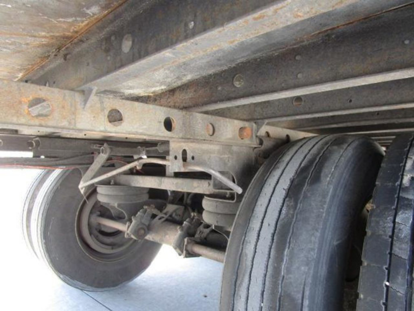 Trailer undercarriage showing dual rear axles and suspension with leaf springs and tires; structural frame and wheel components visible.