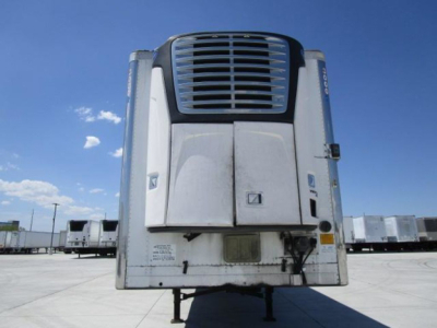 Trailer front view showing large curved grill and two vertical doors with side handles; front mounted refrigeration unit; small label near bottom; blue sky background.