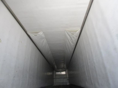 Trailer interior looking down a refrigerated trailer niche with white walls and ceiling, narrow passage, cargo door at far end.