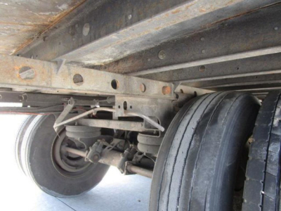 Trailer undercarriage showing dual rear axles and suspension with leaf springs and tires; structural frame and wheel components visible.