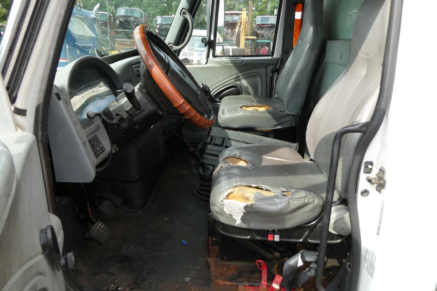 Interior of a 2006 International 4300 SBA cab showing worn seat upholstery and steering wheel with wood trim, dashboard, and entry door.