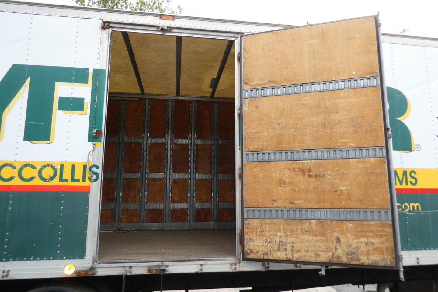 Truck box truck with open rear cargo door showing empty interior cargo space and wooden interior walls.