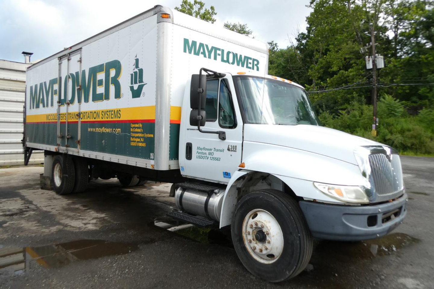 Box truck 2006 International 4300 SBA with Mayflower moving logo on box, white cab, side view showing front grille and wheel. Visible text includes MAYFLOWER on cargo box and company details on door.