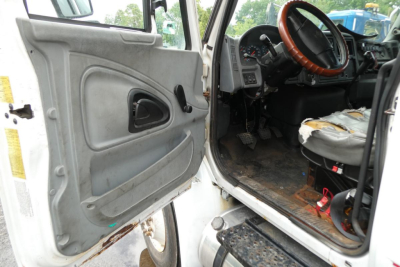 Truck cab interior with open driver door showing steering wheel, dashboard, and worn seat; entry step and door panel visible.