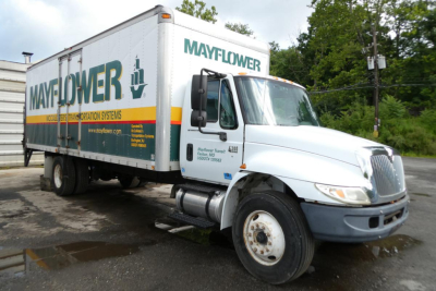 Box truck 2006 International 4300 SBA with Mayflower moving logo on box, white cab, side view showing front grille and wheel. Visible text includes MAYFLOWER on cargo box and company details on door.