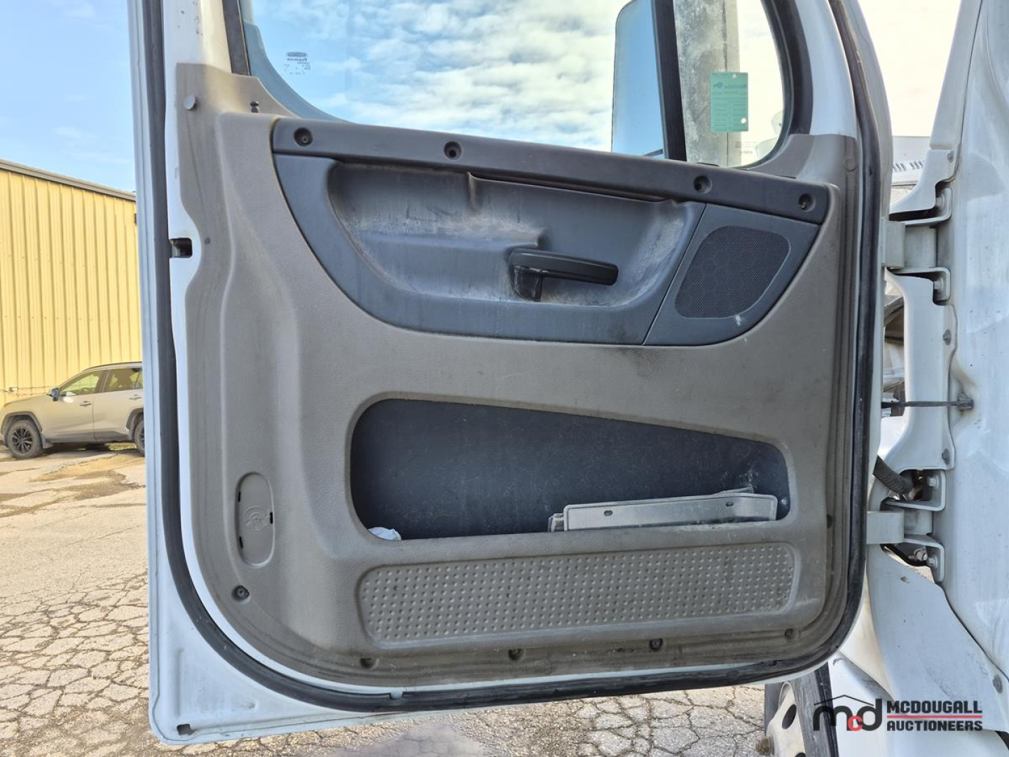 Truck door interior panel with handle and storage pocket visible from cab entry of a Freightliner Cascadia truck.