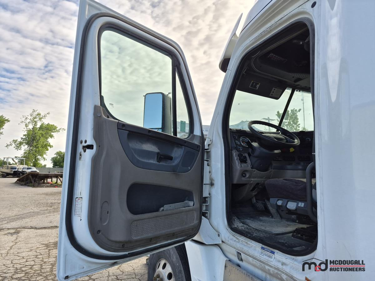 Freightliner Cascadia truck cab interior and open door showing dashboard and steering wheel in view, with VIN label not visible.