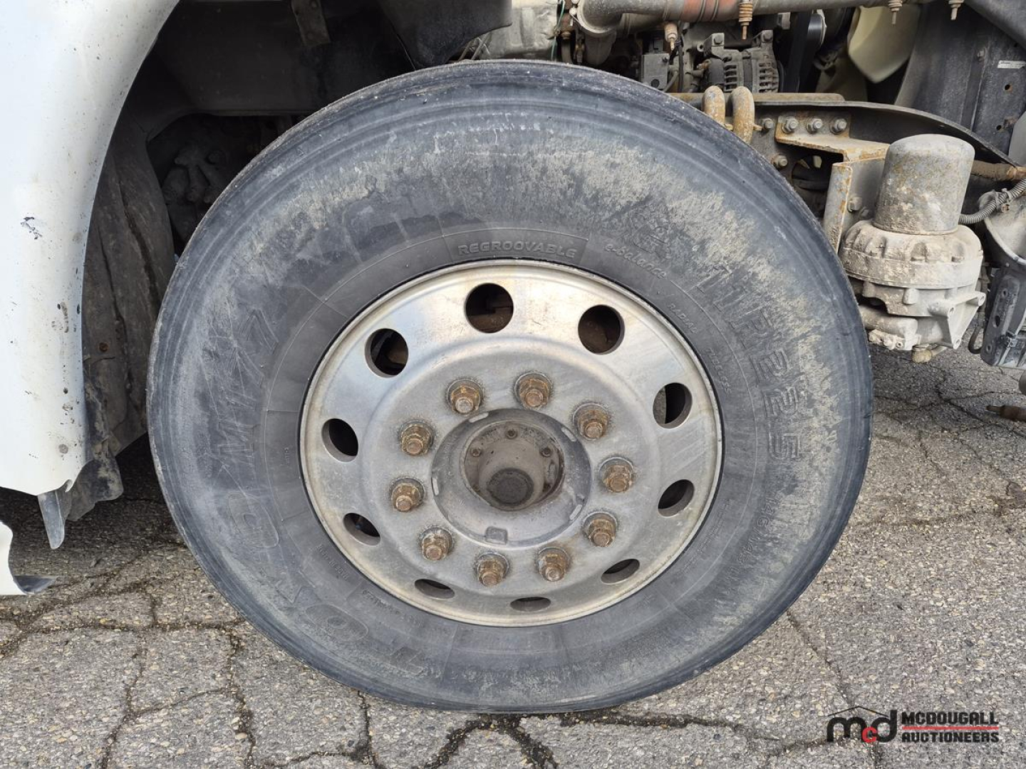 Truck wheel and front axle showing tire and silver steel wheel with lug nuts on Freightliner Cascadia sleeper cab chassis.