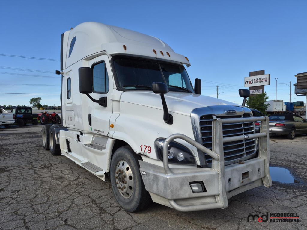 Truck: 2016 Freightliner Cascadia Conventional Sleeper tractor in white, front grille guard, dual rear axles, side mirrors, cab with tall sleeper, VIN plate and numbers on door, dealership lot in background.