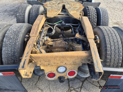 Chassis view of a 2016 Freightliner Cascadia truck showing fifth wheel hitch and rear dual axles with muddy frame and exposed wiring.