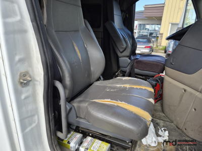 Truck cab interior with worn vinyl seats and torn cushions in Freightliner Cascadia sleeper cab.