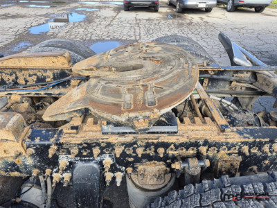 Freightliner Cascadia truck chassis view showing a circular drive shaft cover and mechanical components, with mud and grime on the frame.